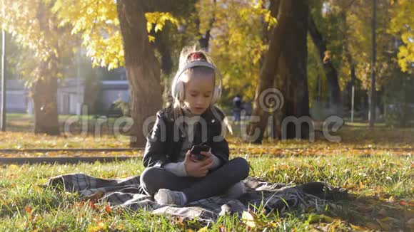 年轻女孩戴着耳机听音乐在秋天的城市公园里唱最喜欢的歌女孩是个了不起的人视频的预览图