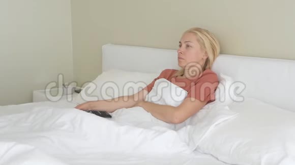 一个女人躺在床上脸上带着一张悲伤的病态她打开电视遥控器视频的预览图