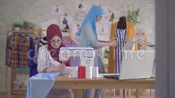 年轻的穆斯林时装设计师戴着国家头巾在缝纫机上工作视频的预览图