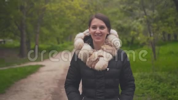 一个穿着暖和的黑色夹克的女孩穿过树林女孩风骚地笑着在框架里调情视频的预览图