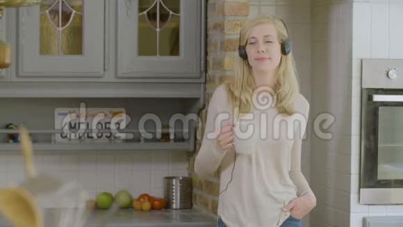 厨房里微笑的女人喝着咖啡跳舞听着耳机里的音乐视频的预览图