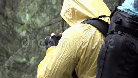 一个年轻人站在树间拍摄夏天森林的侧面景色库存录像穿黄色夹克的徒步旅行者视频的预览图