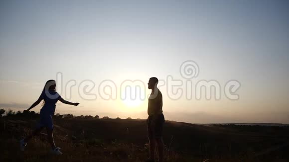 日落时分一对年轻迷人的夫妇在乡村风景中会面留胡子的年轻人和他的女朋友的剪影视频的预览图