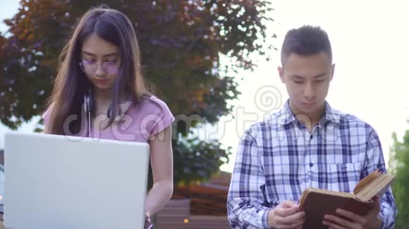 带书的年轻亚裔男学生和带笔记本电脑的年轻亚裔女性视频的预览图