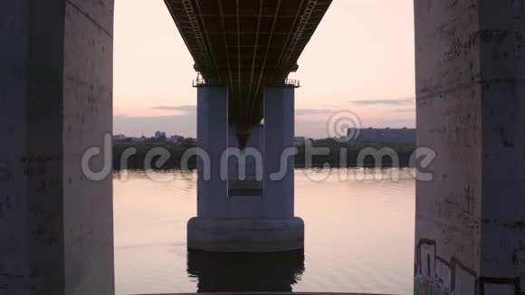 在河桥下的桩间飞来飞去城市背景下横跨宽河的长混凝土桥瓦特的空中观景桩视频的预览图