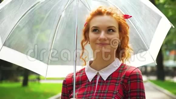 快乐的红头发女孩带着雨伞在阳光明媚的公园里散步视频的预览图