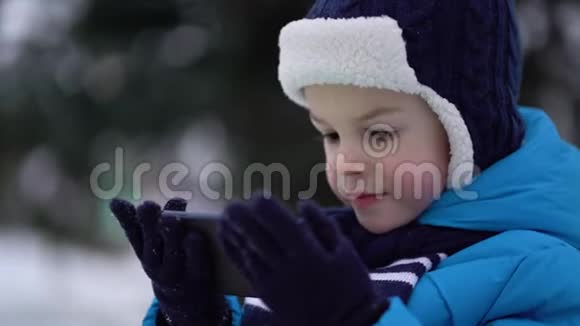 冬天的小男孩在寒冷的雪天穿手机视频的预览图
