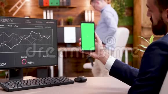 商人拿着绿色屏幕的手机的后视角视频的预览图