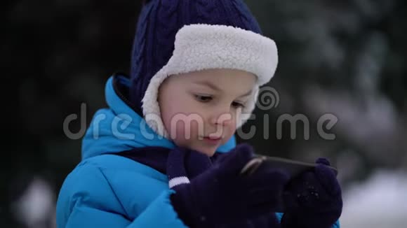 冬天的小男孩在寒冷的雪天穿手机视频的预览图