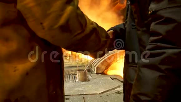 两名炼钢工人在热厂电弧炉前铸锭时握手后景冶金视频的预览图