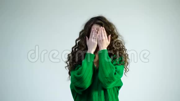 白色背景上戴着牙套的搞笑情绪女人的肖像女孩用穿绿色衣服的手遮住眼睛视频的预览图