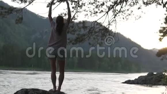 日落时分一位妇女在河边的石头上跳舞视频的预览图