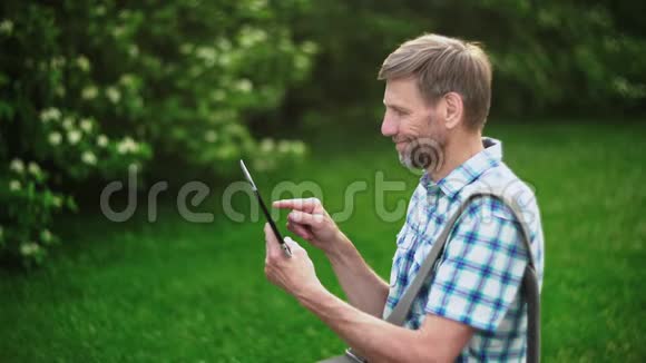 成熟男人在绿色自然背景下浏览数码平板电脑视频的预览图