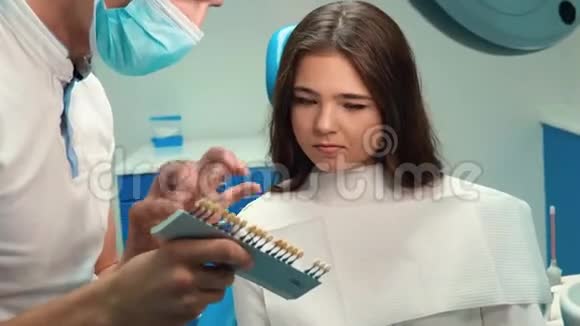 戴手套的英俊牙医去除牙釉质刻度以便在预约时为黑发患者妇女取合适的阴影视频的预览图
