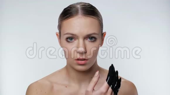 可爱的女人涂化妆品面膜泥浆特写看相机白色背景4K视频的预览图