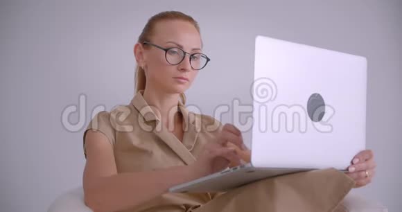 优雅的白种人女商人坐在扶手椅上用笔记本电脑打字在白色的办公室里体贴入微视频的预览图