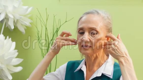 高级女性在家庭浴室做面部按摩化妆品课程中的成熟女性面部皮肤按摩视频的预览图
