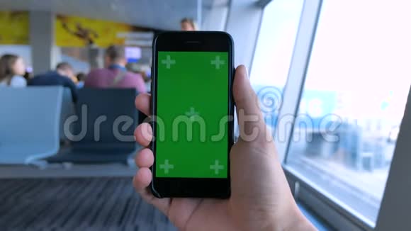 在国际机场背景下关闭带有绿色屏幕色度键的人持有智能手机视频的预览图