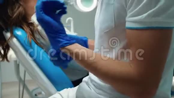 戴着医疗手套和戴着眼镜的年轻牙医准备检查年轻的黑发女人病人调整他的身体视频的预览图