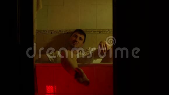 一个男人穿着衣服坐在浴室里一个体贴悲伤的人坐在浴室里灯光昏暗视频的预览图