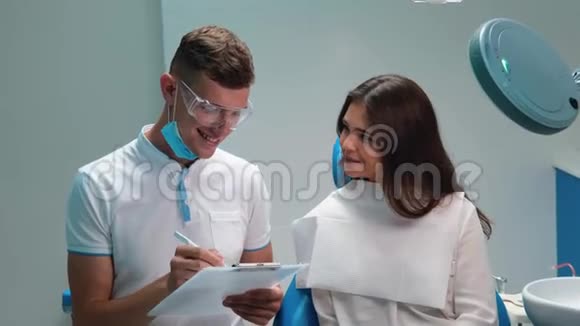 年轻英俊的牙医在去诊所检查后向美丽的黑发女子解释治疗计划视频的预览图