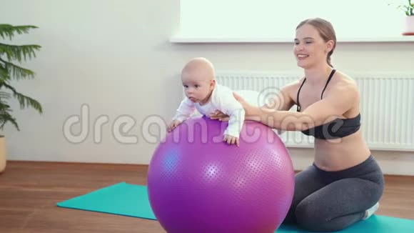 快乐的妈妈在玩婴儿在大球上做婴儿健身运动视频的预览图