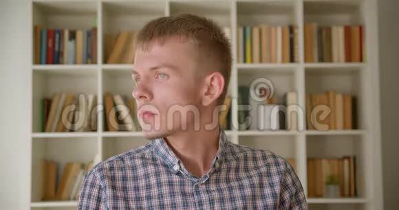 白种人图书管理员在书架背景上平静而害羞地观看镜头的肖像视频的预览图