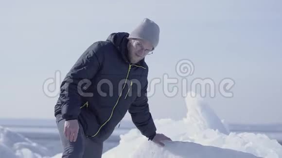 年轻的胡子帅哥穿着温暖的夹克帽子和靴子爬上冰川神奇的自然雪冰川这就是视频的预览图