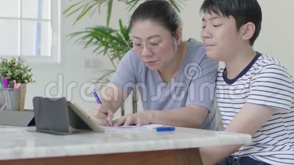 严格的亚洲母亲正在检查儿子家庭作业视频的预览图