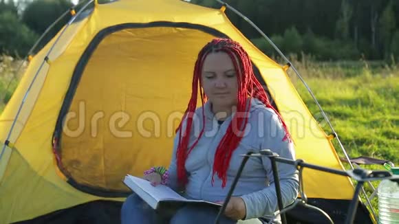一个女人在篝火帐篷附近戴着非洲辫子看着一个沸腾的锅视频的预览图