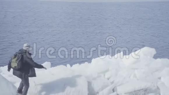 年轻的金发胡子帅哥穿着温暖的夹克帽子和靴子爬上冰川走在边缘令人惊叹视频的预览图