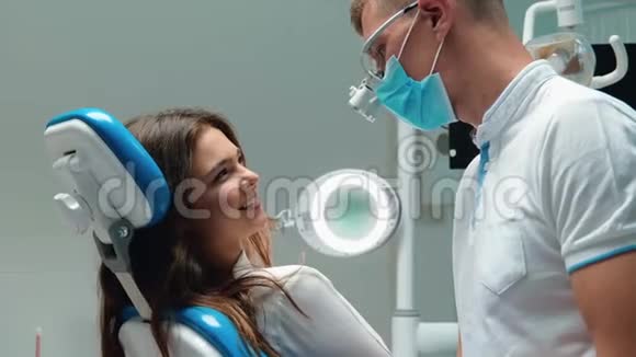 戴着医用手套和口罩的年轻牙医检查年轻的黑发女性病人询问她的牙齿问题视频的预览图