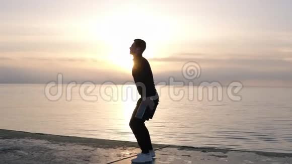 迷人的运动的高个子穿着短裤在靠近大海的木地板上热身做仰卧起坐和跳跃视频的预览图