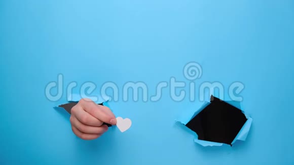 靠近女性的手把白色的小心脏通过并显示一个好的标志撕裂的蓝色纸墙视频的预览图
