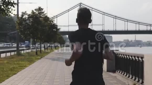 年轻苗条男子在城市码头沿河奔跑的背面景色肌肉活跃的男孩跑得很快运动员沿着河跑视频的预览图