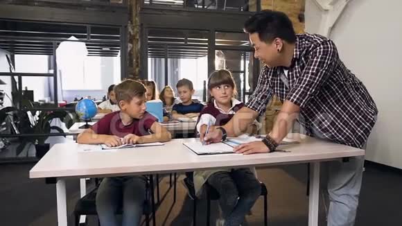 年轻的韩国男教师帮助小学生在课堂上学习功课视频的预览图