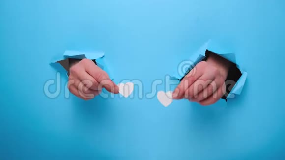女人的手通过撕裂的蓝色纸墙抱着白色的小心脏视频的预览图
