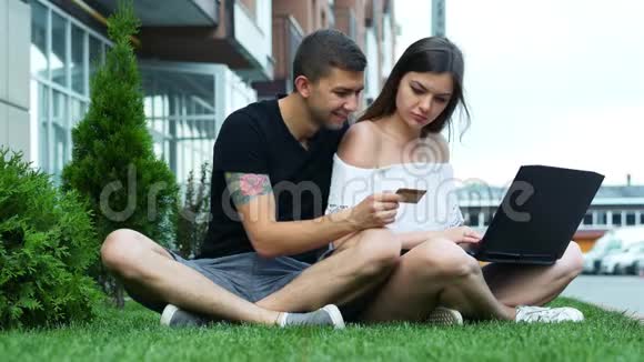 快乐夫妇使用笔记本电脑进行网上购物选择商品并在草地上输入信用卡号码视频的预览图