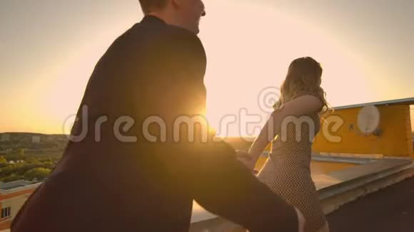 年轻夫妇牵着手走着女人牵着男朋友在屋顶的建筑日落POV概念视频的预览图