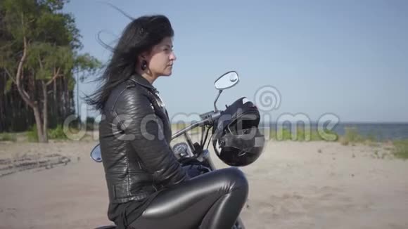 侧面看坐在摩托车上的女孩望着河岸爱好旅游和积极的生活方式视频的预览图