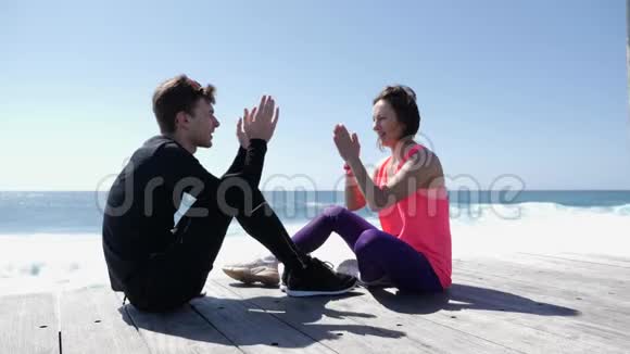 快乐的年轻男友和女友坐在海边玩击掌游戏波浪溅落在岩石上奴隶视频的预览图