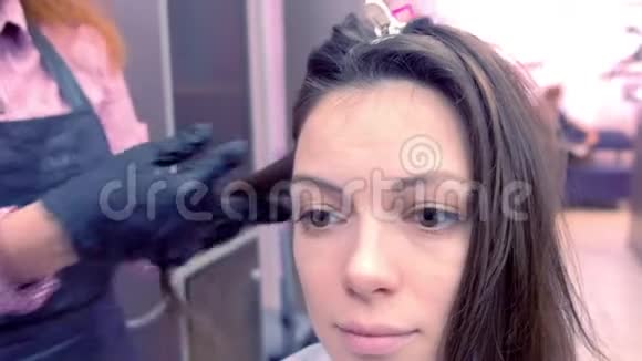 美容师准备在美容院用发钳给美女扎黑棕色头发视频的预览图