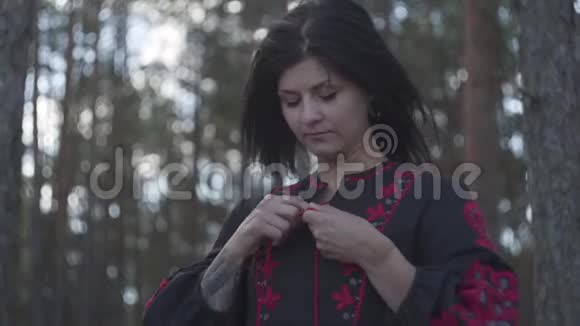 美丽的年轻女子把花边系在一件黑色和红色的裙子上站在松林的树下的肖像视频的预览图