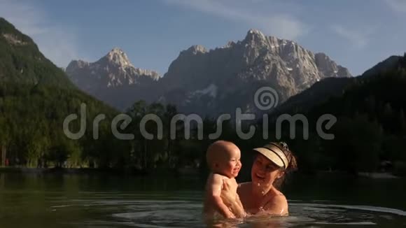 幸福的家庭妈妈和宝宝在一个温暖的山湖里游泳背景是高高的雪山母亲节视频的预览图