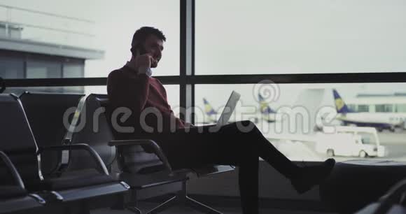一个漂亮的年轻人在机场打电话同时他合上笔记本去拿视频的预览图