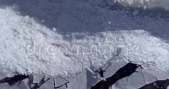 鸟瞰年轻活跃的快乐男子行走在冰冰冰川附近的冬季海洋海岸线无人视野视频的预览图