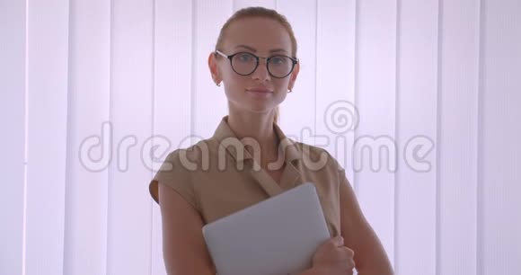 优雅的白种人女商人拿着笔记本电脑手表进入相机专注而平静地站在窗户附近视频的预览图
