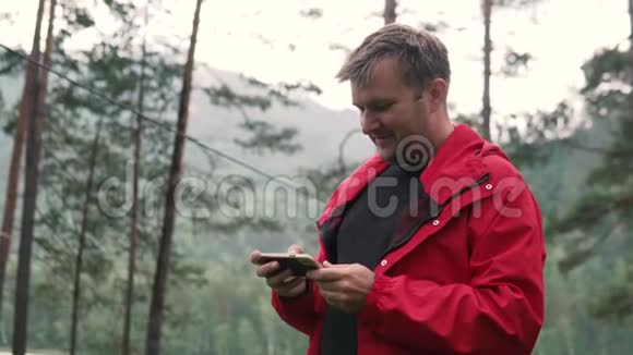 一个人在河边的森林里看手机视频的预览图