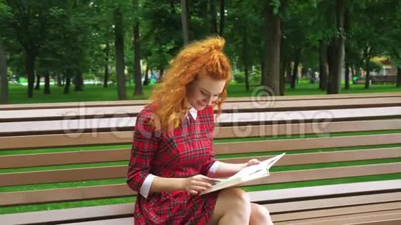 可爱的红头发女孩在公园里读有趣的书视频的预览图