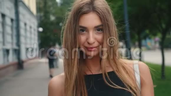 一个穿着红唇黑裙的性感女人看着镜头微笑着走在城市的大街上视频的预览图